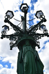 Fototapeta na wymiar An ancient and big lamppost in Castle square in Prague, in Czech Republic, with blue sky and white clouds in the background, decorated with statues and lanterns.