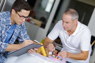 Man testing electronics, another noting results