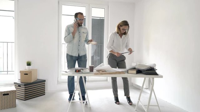 Two architects with tablet, cellphone and blueprints working at their new home
