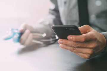 close up of smart medical doctor working with mobile phone and stethoscope on dark wooden desk
