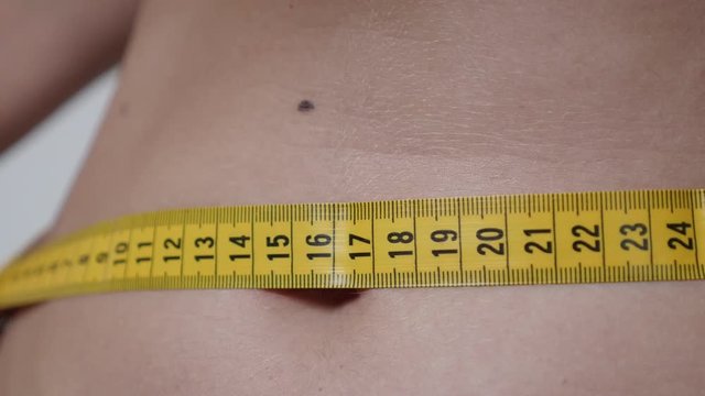 Measuring of female waist size close-up 4K 2160p 30fps UHD footage - Woman belly and yellow tape shallow DOF 3840X2160 UltraHD video