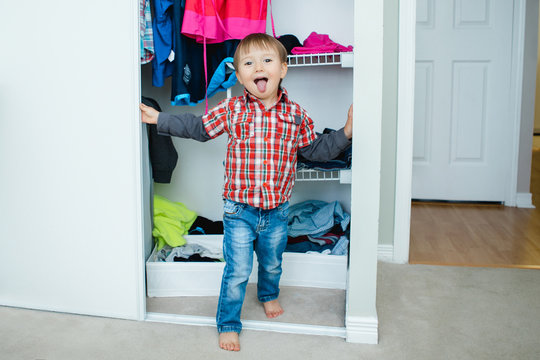 Candid Natural Portrait Of Funny Cute White Caucasian Little Boy Toddler In Wardrobe At Home Making Funny Face Showing Tongue, Lifestyle Documentary Style