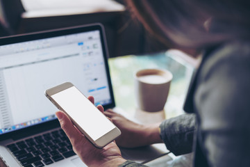 Mockup image of business woman holding mobile phone with blank white screen with latop on wooden table in cafe