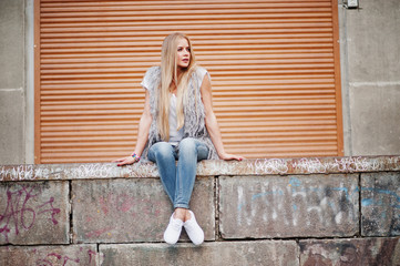 Stylish blonde woman wear at jeans and girl sleeveless with white shirt against shutter background. Fashion urban model portrait.