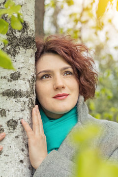 Pretty young red head woman close to the tree in spring park. Spring trees background.