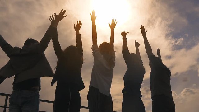 silhouette of people rejoicing and lifting up his hands. a group of successful businessmen happy and celebrate the victory on the roof of the business center. slow motion