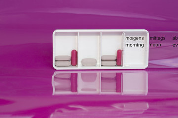 Daily ration of medication in white tablet box on pink background 