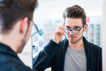 Man testing glasses in optician shop mirror