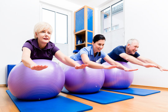 Physio Showing Senior Couple How To Use Gym Ball For Exercises