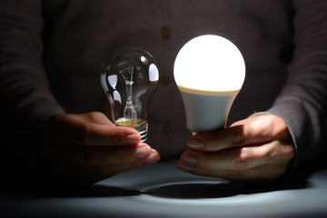 Female hands holding a glowing led and incandescent bulbs in the dark