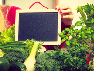 Woman having green vegetables holding board