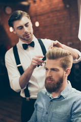 Fototapety  Fryzjer szykownie ubrany przystojny stylista robi idealną fryzurę brodatemu facetowi w stroju caual jeans. Zarówno skoncentrowany, jak i poważny