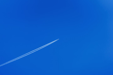 Flying airplane leaving diagonal trace on a clear blue sky without clouds. Copy space for your text, modern background, pattern, wallpaper or banner design