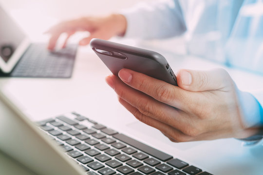 Close Up Of Businessman Using Mobile Phone And Laptop Computer On White Desk In Modern Office