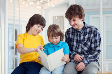 Obraz premium 3 boy read book outdoors on swing