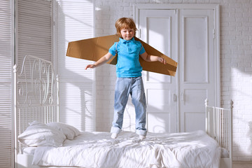 Fototapeta na wymiar Happy boy with cardboard boxes of wings in home dream of flying