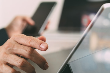 close up of businessman hand working with smart phone and laptop and digital tablet computer in modern office