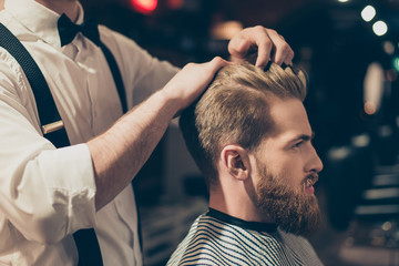 Attractive classy dressed barber shop hairdresser is turning client`s head to present his work for him. Stunning! Hairdo looks trendy and so perfect