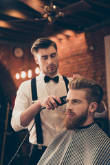 Beard styling for a handsome young guy at the barber shop. Hairdresser is attractive and wearing classic outfit, he is focused and serious © deagreez