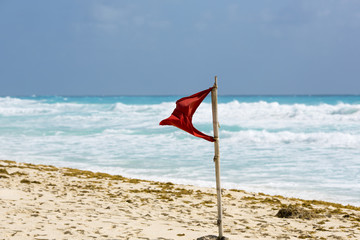 Red flag waving on the beach. Sunny day and strong wind. Dangerous to swim or surf.