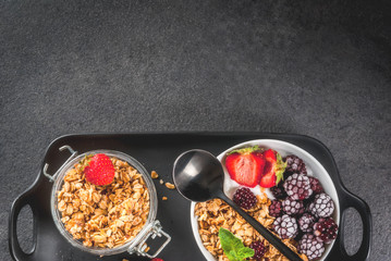 Healthy breakfast. Summer berries and fruits. Homemade Greek yogurt with granola, blackberries, strawberries and mint. On a black stone table, with the ingredients. Top view copy space