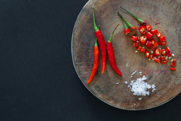 Red hot chili peppers and sliced peppers on a wooden cutting board with salt crystals nearby on a black background. Asian species.