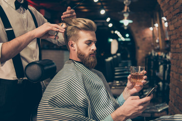 Chill out at the barber shop. Side view of handsome young red bearded man drinking scotch and...