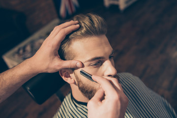 Close up of a hairdresser`s work for an attractive young blond man at the barber shop. He is doing styling of his beard, shaving it with straight razor © deagreez