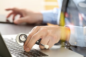 close up of smart medical doctor working with laptop computer and stethoscope on dark wooden desk