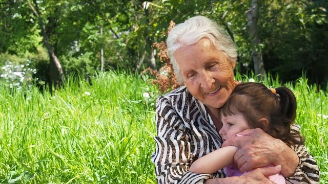 A happy grandmother hugs a child. An elderly woman with a child outdoors.