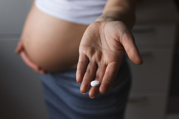 belly of pregnant woman and vitamin pills in the hand