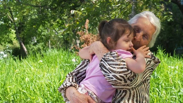 A happy grandmother hugs a child. An elderly woman with a child outdoors.