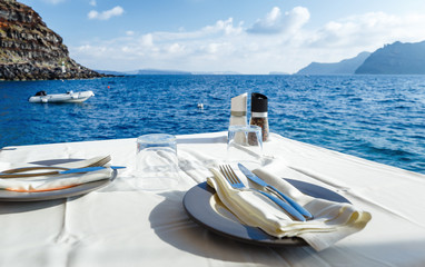 Served table with white tablecloth against blue water of Aegean sea on Santorini island resort in Greece, Europe.