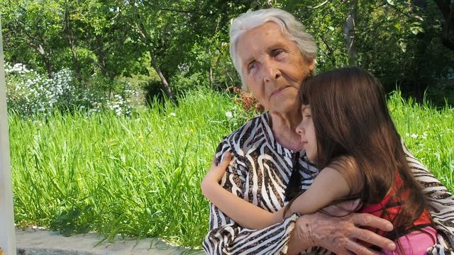 Grandmother with granddaughter. A happy grandmother hugs her granddaughter. An elderly woman with a child outdoors.