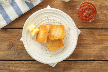 Plate with tasty garlic French bread slices on wooden table