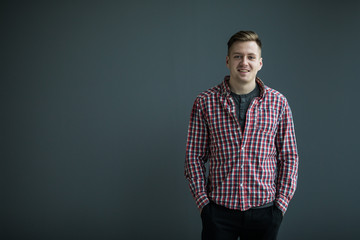 Handsome young man in smart casual wear looking at camera and holding hands in pockets while standing against grey background