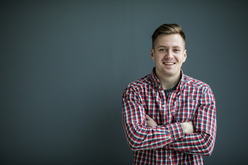 Portrait of handsome young man in casual shirt keeping arms crossed and smiling while standing against grey background