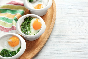 Bowls with tasty eggs and spinach on wooden table