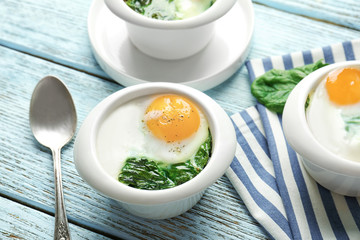 Bowls with tasty eggs and spinach on wooden table