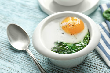 Bowl with tasty egg and spinach on wooden table