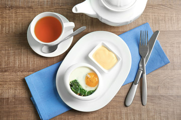 Plate with tasty egg and spinach on wooden table
