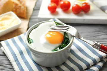 Bowl with tasty egg and spinach on wooden table