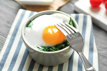 Bowl with tasty egg and spinach on wooden table