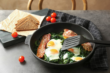 Frying pan with tasty eggs, spinach and bacon on table