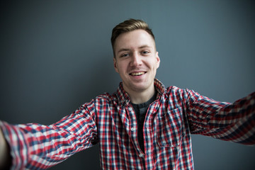 Top view of handsome young man in hat and sunglasses making selfie and smiling while standing against grey background