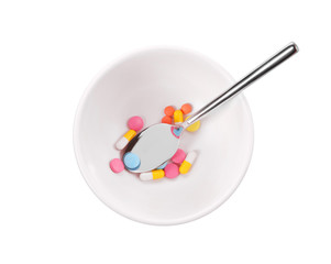 Diet concept. Spoon in bowl with assorted pills on white background