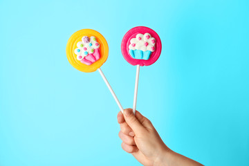 Female hand with tasty lollipops on color background
