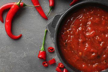 Pan with tasty chili sauce on grey textured table, closeup