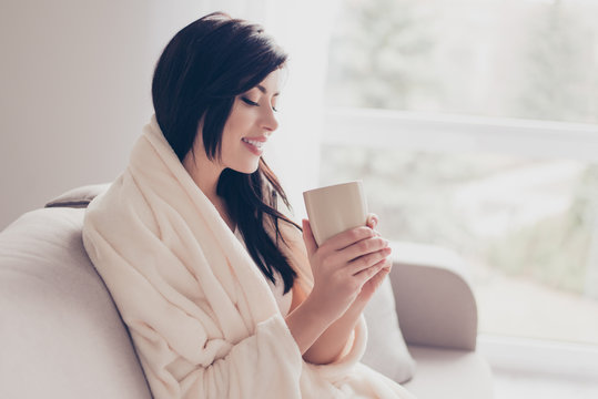 Morning is here! Close up profile portrait of cute brunette girl, smiling and holding a cup of coffee, covered with a plaid. Nice beginning of day