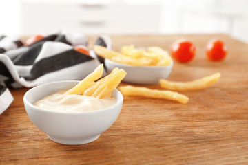 Bowl with tasty mayonnaise sauce and French fries on wooden table